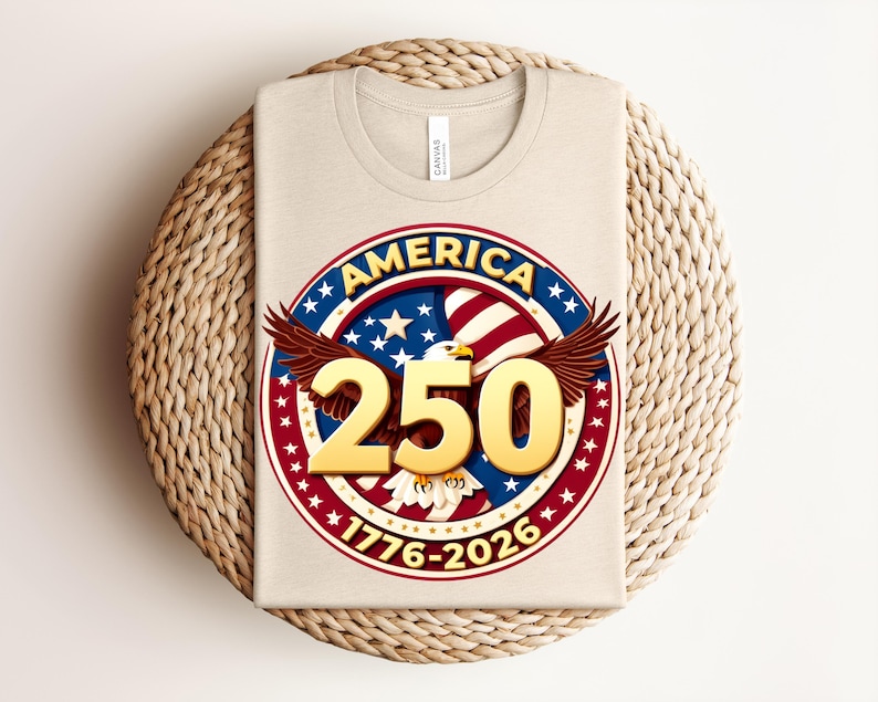 May include: A beige t-shirt with a circular design. The design features the word "AMERICA" in blue, red, and white, a golden "250", and an eagle with outstretched wings. The dates "1776-2026" are also displayed on the shirt.