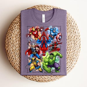 May include: A purple t-shirt with a vibrant graphic of Marvel superheroes, such as Iron Man, Captain America, Spider-Man, Thor, Wolverine, Hulk, and Deadpool. The shirt is folded on a circular woven mat.