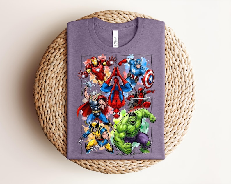 May include: A purple t-shirt with a vibrant graphic of Marvel superheroes, such as Iron Man, Captain America, Spider-Man, Thor, Wolverine, Hulk, and Deadpool. The shirt is folded on a circular woven mat.