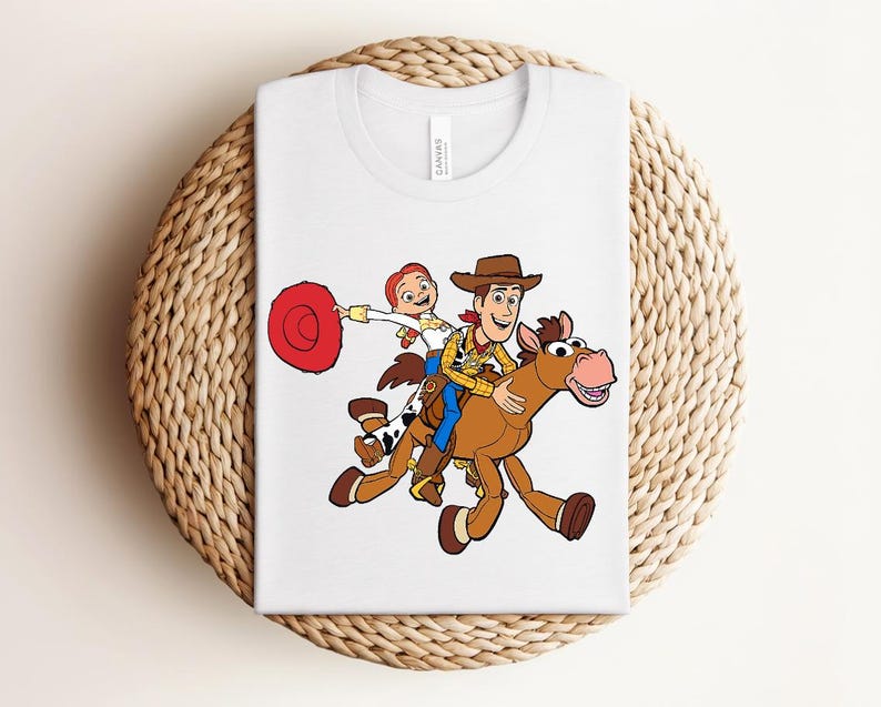 May include: White t-shirt featuring a colorful graphic of Woody and Bullseye from Toy Story. Woody is riding Bullseye, with Jessie holding a red lasso. The design is centered on the shirt.