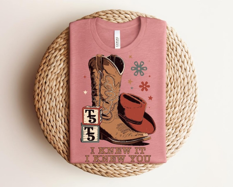 May include: A dusty rose t-shirt featuring a graphic of a brown cowboy boot, a brown cowboy hat, and two stacked alphabet blocks with the letter T. The text I KNEW IT I KNEW YOU is printed below the graphic, along with small star and flower icons.