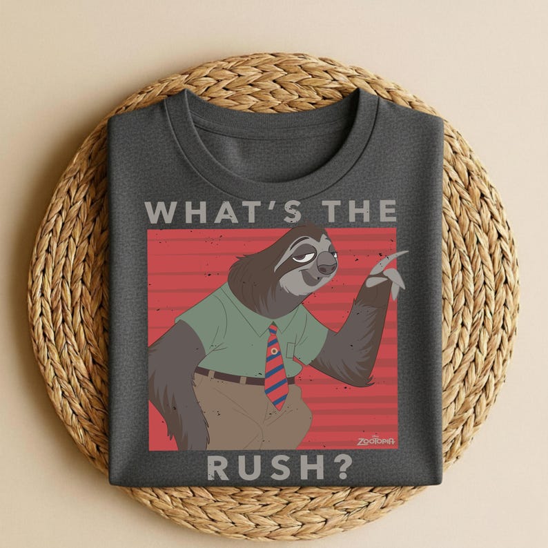 Puede incluir: Camiseta gris oscuro con un perezoso de dibujos animados con una camisa verde, pantalones marrones y una corbata a rayas rojas y azules. El texto "WHAT'S THE RUSH?" se muestra arriba y abajo de la ilustraci&oacute;n.