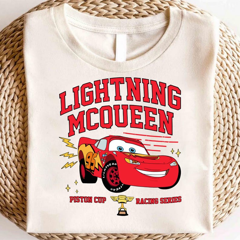 May include: A white t-shirt with a red and black graphic of Lightning McQueen from the Cars movie. The graphic includes the text "Lightning McQueen", "Piston Cup", and "Racing Series".