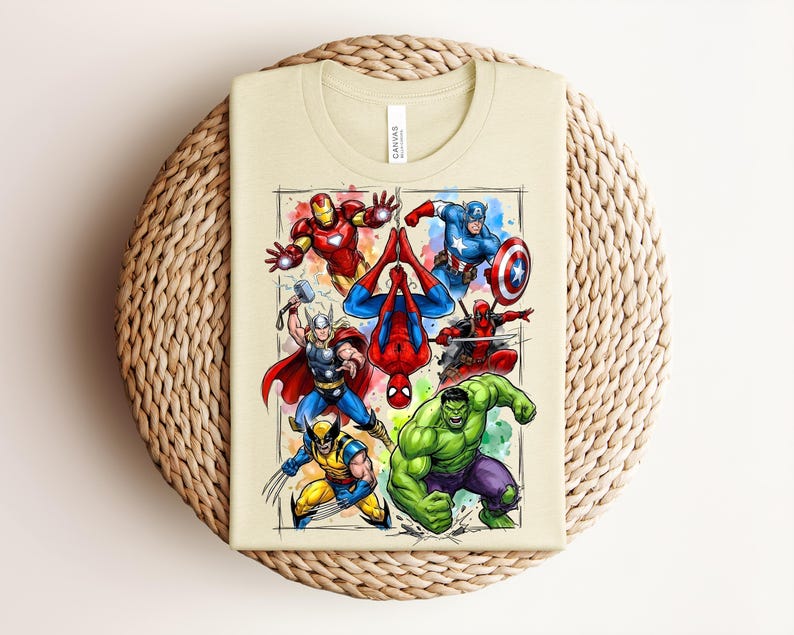 May include: A beige t-shirt displaying a vibrant graphic of Marvel superheroes such as Iron Man, Captain America, and Spider-Man. The design, with a watercolor effect, features the characters in action. The t-shirt is folded on a woven, circular mat.