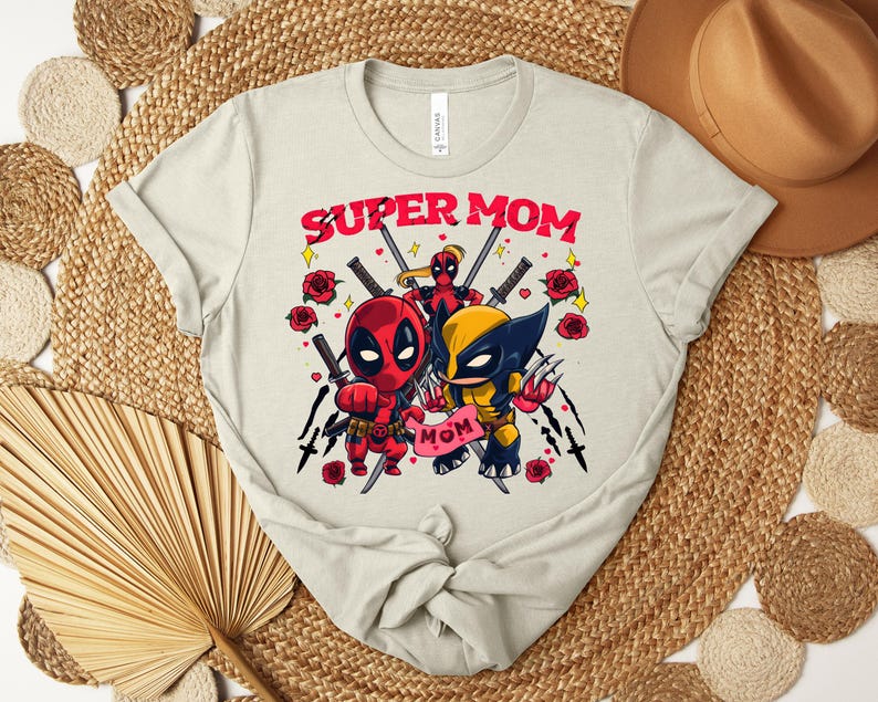 K&ouml;nnte beinhalten: Hellbeige T-Shirt mit einer Grafik von Deadpool und Wolverine und dem Text "SUPER MOM". Das Design umfasst rote Rosen und Schwerter. Das T-Shirt ist aus weichem Material.