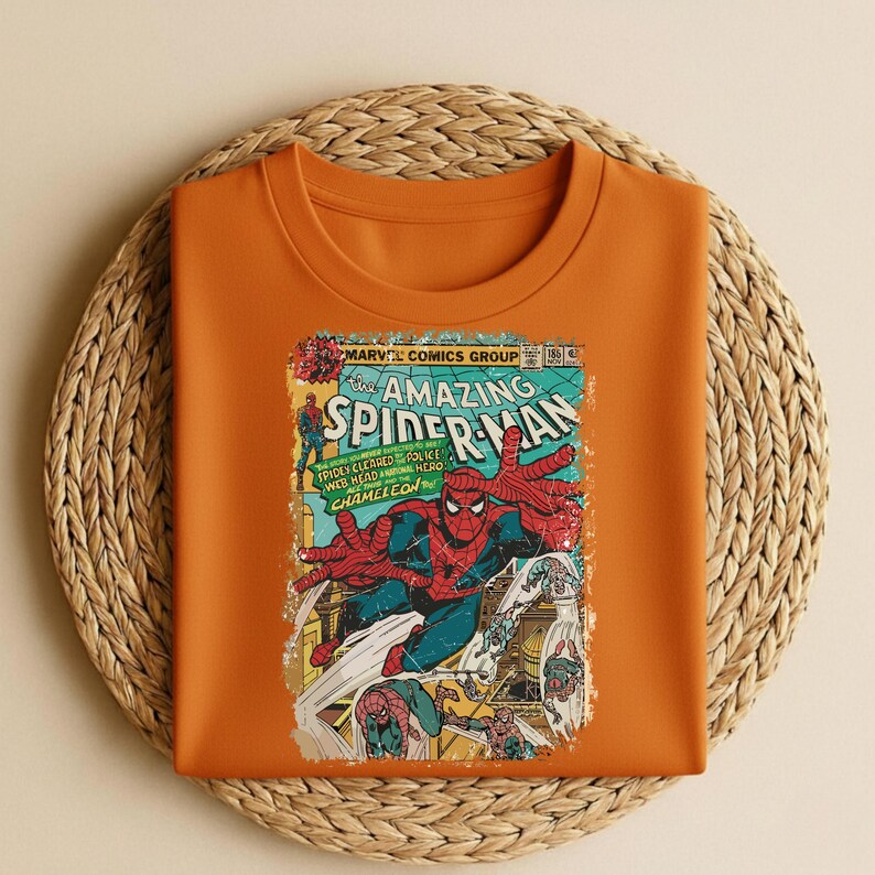 May include: Orange crew neck sweatshirt featuring a vintage comic book cover of Spider-Man. The comic book art includes the title "Amazing Spider-Man" and the text "Spider Cleared Police Web Head Hero Chameleon". The artwork is in red, blue, and yellow.