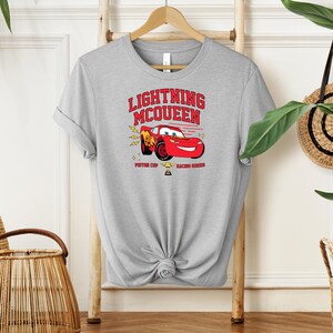 May include: Gray t-shirt with a red cartoon race car and the text "Lightning McQueen Piston Cup Racing Series".
