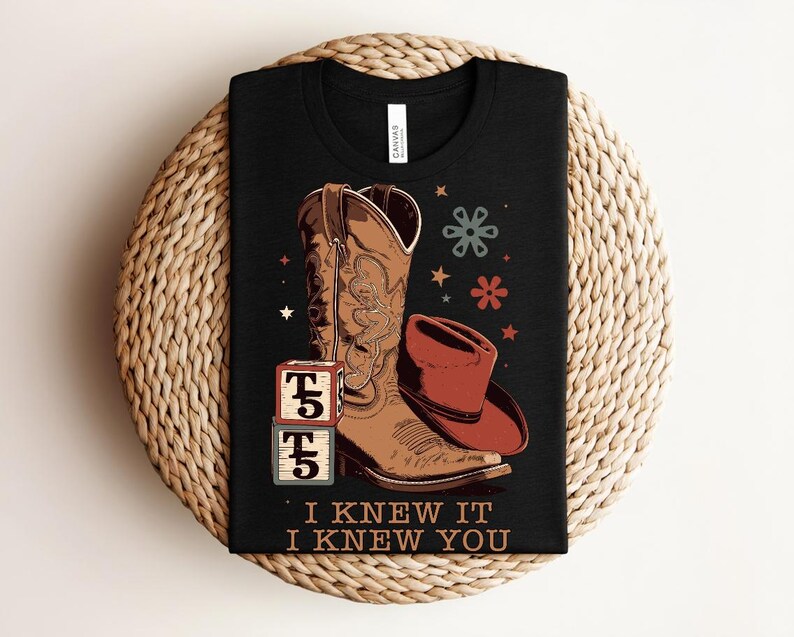 May include: A black t-shirt featuring a graphic of a brown cowboy boot, a red cowboy hat, two stacked blocks with the text T5, and small star and flower icons. The text I KNEW IT I KNEW YOU is printed in a tan font at the bottom of the graphic.
