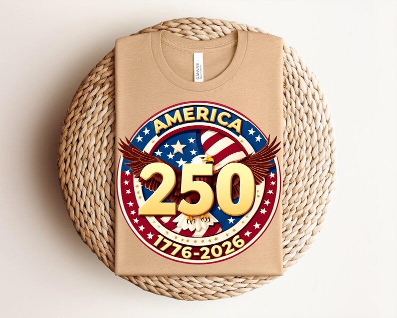 May include: A folded tan t-shirt with a circular graphic. The graphic features the word "AMERICA" in blue, a red and white striped background, stars, and the number "250" in gold. The design includes an eagle and the dates "1776-2026".