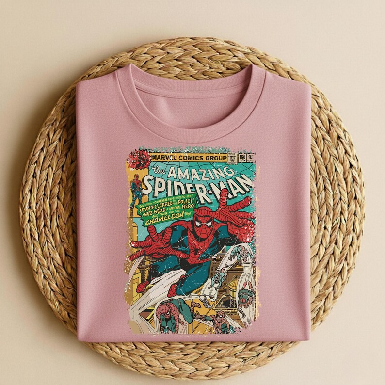 May include: A light pink crew neck sweatshirt featuring a vintage comic book cover of Spider-Man. The comic book art is in shades of red, blue, yellow, and green, with the words "The Amazing Spider-Man" prominently displayed.