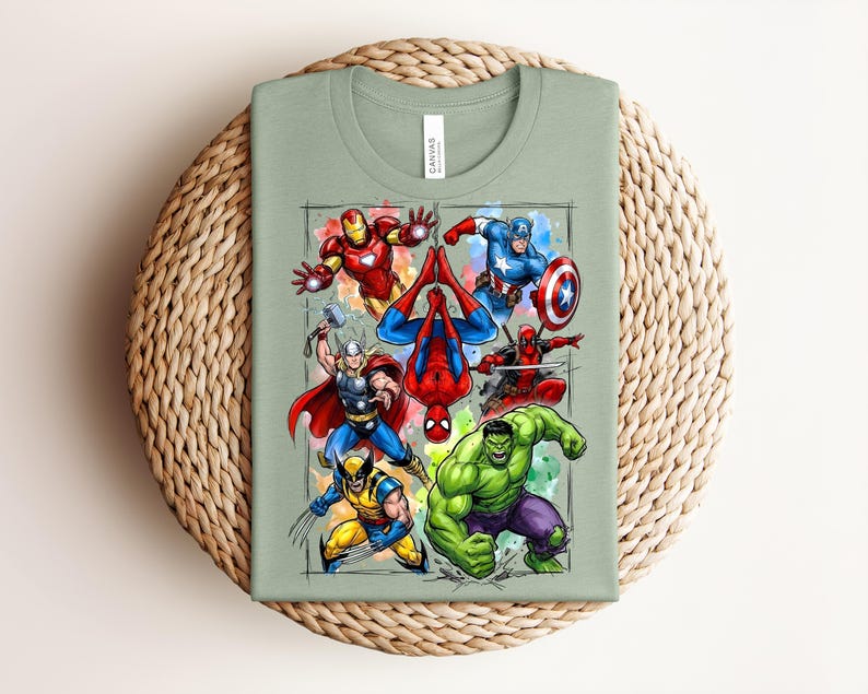May include: A sage green t-shirt with a vibrant graphic of superheroes such as Iron Man, Captain America, Thor, Spider-Man, Wolverine, Deadpool, and the Hulk. The design has a watercolour effect and is set within a rectangular frame.