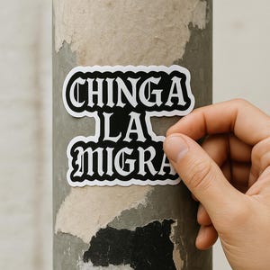 Può includere: Un adesivo in bianco e nero con le parole "CHINGA LA MIGRA" in un carattere gotico. L'adesivo viene applicato a un palo grigio usurato. L'adesivo ha un bordo bianco.