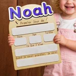 May include: Wooden sign with the name "Noah" in blue letters. The sign has spaces to record information about a child's first day, including date, age, and height. The text "Premier Jour de" is also visible.