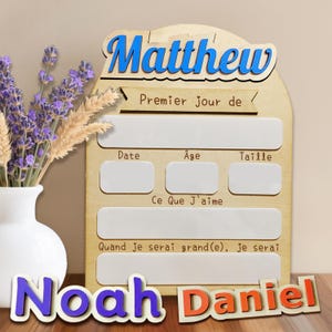 May include: A wooden sign with the name "Matthew" in blue, and the words "Premier jour de" above three blank boxes labelled "Date", "&Acirc;ge", and "Taille". Below are the words "Ce Que J'aime" and "Quand je serai grand(e), Je serai". The name "Noah Daniel" is at the bottom.