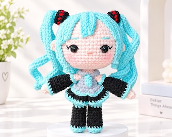 May include: A crocheted doll with light blue hair styled in twin tails featuring black and red hair ties. The doll has a pale pink face, black eyes, and wears a grey and light blue top with black sleeves and black pants with light blue cuffs.