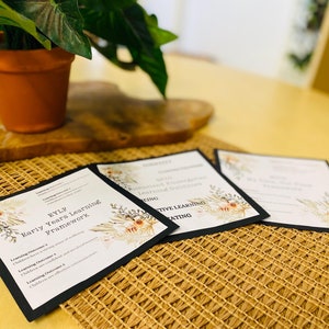 May include: Three educational documents with black borders and floral designs are displayed on a woven mat. The documents feature text related to early childhood education, including "EYLF Early Years Learning Framework". A potted plant sits in the background.