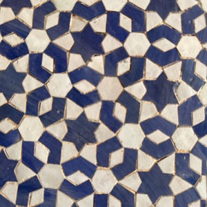 Op de afbeelding: Close-up van een mozaïektegelpatroon. Het ontwerp heeft een herhalend geometrisch patroon van blauwe en witte ster- en ruitvormen. De tegels zijn gerangschikt in een complex, in elkaar grijpend ontwerp.