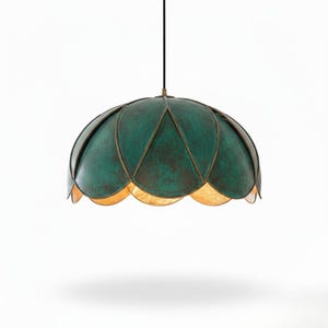 May include: A hanging pendant light with a green, petal-shaped shade. The shade has a textured finish and is trimmed with a gold-colored metal. The light hangs from a black cord, casting a warm glow from the scalloped bottom edge. Home decor.