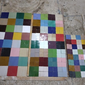 Pode incluir: Três tábuas de madeira exibindo uma variedade de pequenas telhas quadradas e coloridas. As telhas são dispostas em um padrão de grade, mostrando uma mistura de cores, incluindo azul, verde, vermelho, amarelo e branco. As tábuas variam em tamanho.