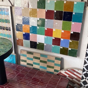 Pode incluir: Uma exposição de azulejos quadrados coloridos em várias tonalidades, incluindo azul, verde, vermelho e amarelo. Os azulejos estão dispostos numa parede, mostrando uma gama de opções de design. Várias mesas com superfícies de azulejos também são visíveis.