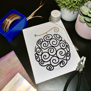 May include: A black and white line drawing of a swirl pattern on a white background. The drawing is on a piece of paper with a silver chain next to it.