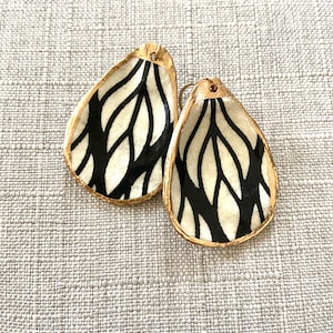 May include: A pair of black and white ceramic earrings with a gold rim. The earrings are shaped like teardrops and have a wavy pattern.