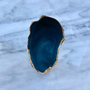May include: A blue agate bowl with a gold rim. The bowl is on a white marble surface.
