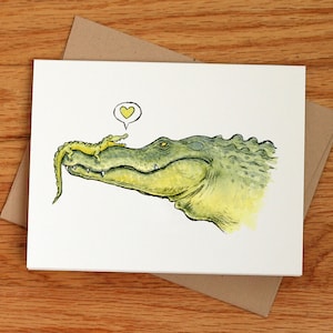 May include: A watercolor illustration of a green alligator with a smaller alligator on its snout. A yellow heart is above the alligators.