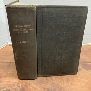 May include: A dark gray hardcover book titled Annual Report of the Chief of Engineers U.S. Army Part 3 1918. The book features a plain front cover with a simple embossed border and gold lettering on the spine indicating the title and year.