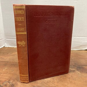 May include: A hardcover book titled Reinforced Concrete by Caughey with a deep red fabric cover. The spine features gold lettering and a small gold graphic. The front cover has the title and author embossed in the center of the red material.