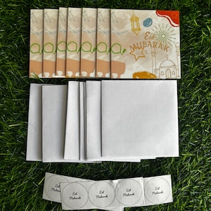 Puede incluir: Un conjunto de seis tarjetas de felicitaci&oacute;n en blanco con sobres y pegatinas. Las tarjetas son de color beige con un borde marr&oacute;n claro. Los sobres son blancos. Las pegatinas son redondas y blancas con el texto "Eid Mubarak" en negro. Las tarjetas presentan una ilustraci&oacute;n colorida de una mezquita, linternas y estrellas.