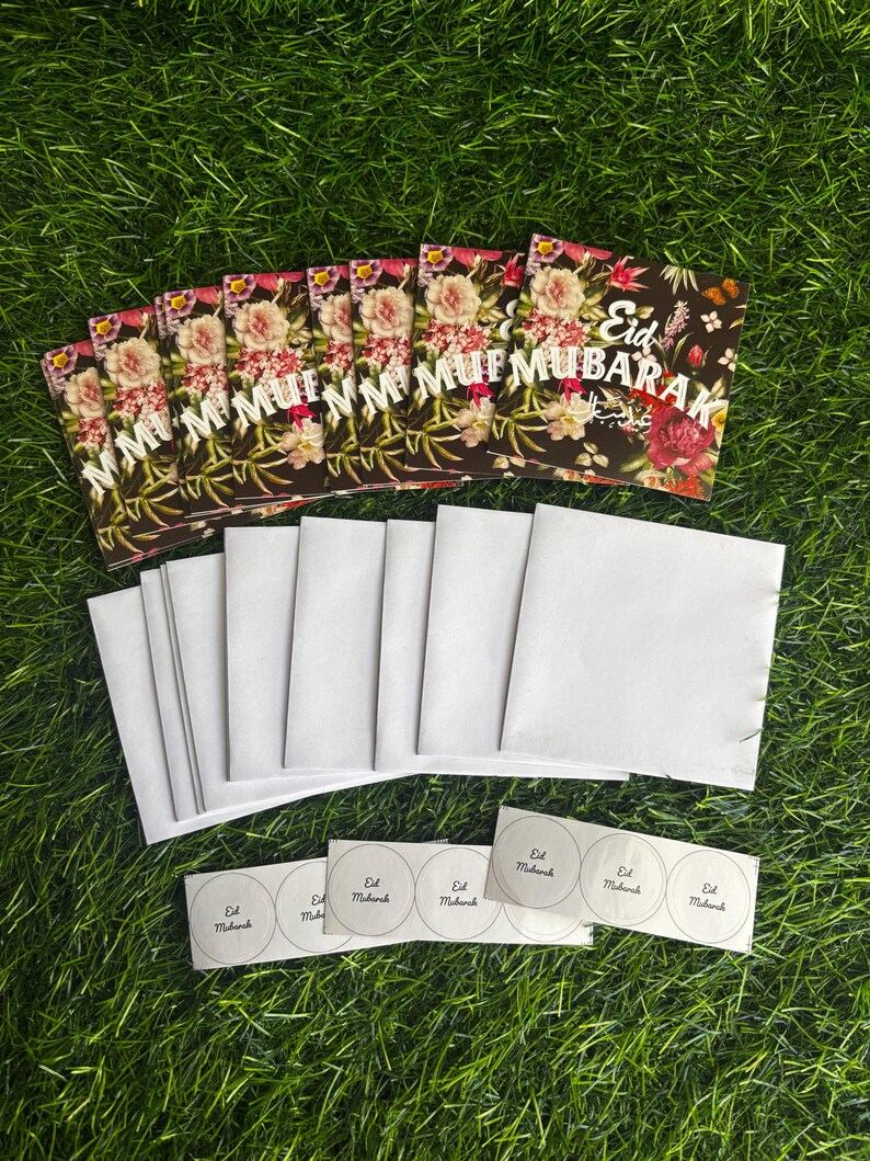 Puede incluir: Un conjunto de 10 tarjetas de felicitaci&oacute;n florales con el texto "Eid Mubarak" en letras blancas sobre fondo negro. Las tarjetas se acompa&ntilde;an de 10 sobres blancos y 5 pegatinas redondas con el texto "Eid Mubarak" en letras negras.