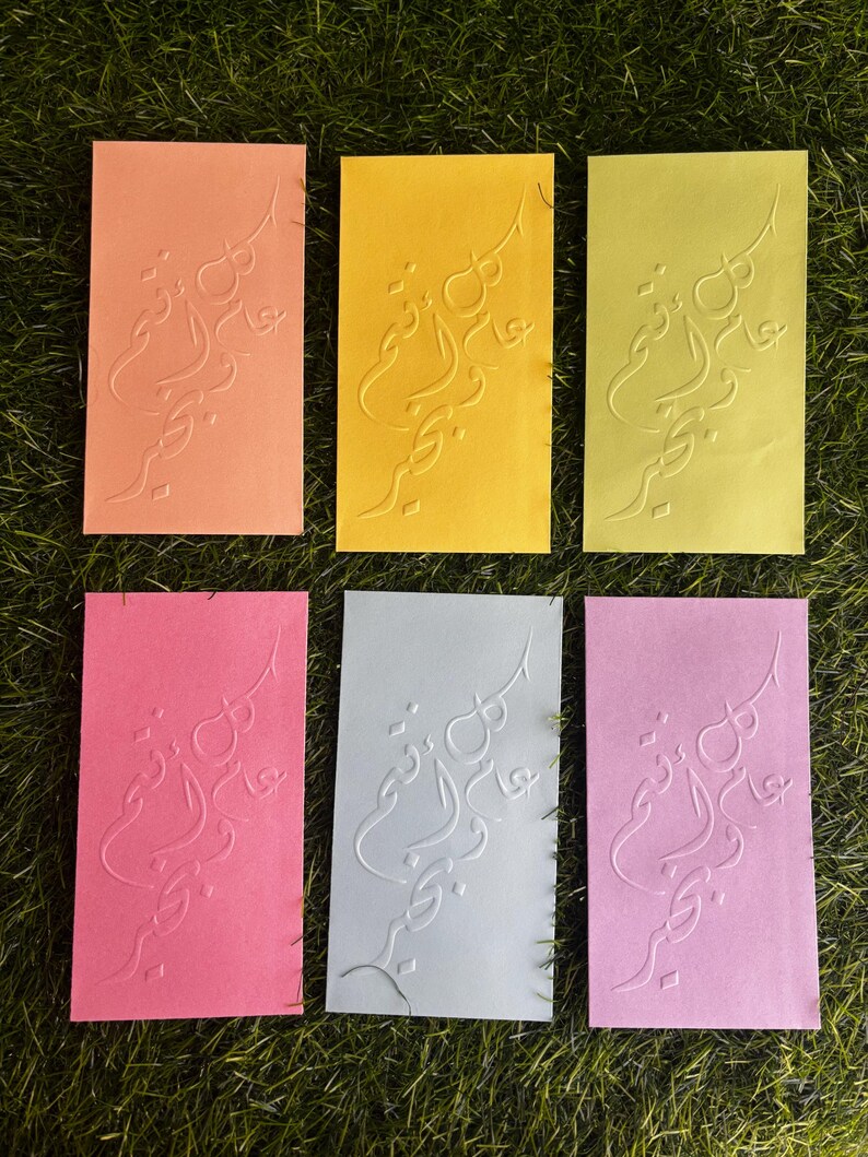 Puede incluir: Seis tarjetas de felicitaci&oacute;n en blanco con un dise&ntilde;o en relieve en escritura &aacute;rabe. Las tarjetas son de varios colores: naranja, amarillo, verde, rosa, azul claro y morado claro.