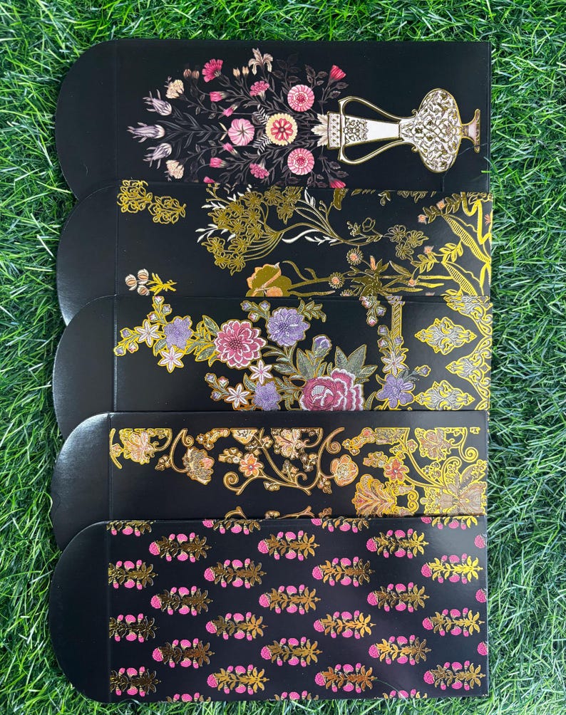 Puede incluir: Cinco sobres negros con dise&ntilde;os florales dorados y rosados. Los sobres tienen esquinas redondeadas y est&aacute;n decorados con patrones intrincados.
