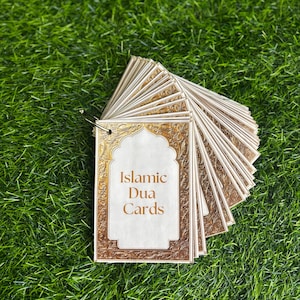 May include: A set of Islamic Dua Cards with a gold and white design. The cards are stacked and have a ring attached to the top. The text on the front of the cards reads "Islamic Dua Cards".