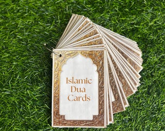 Puede incluir: Un juego de cartas de Dua islámicas con un diseño dorado y blanco. Las cartas están apiladas y tienen un anillo en la parte superior. El texto en la parte frontal de las cartas dice "Islamic Dua Cards".