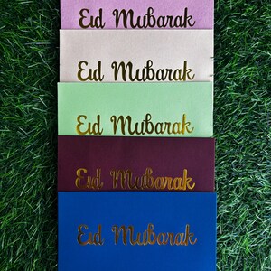 Puede incluir: Cinco sobres de diferentes colores con el texto "Eid Mubarak" escrito en letras doradas. Los sobres est&aacute;n apilados uno encima del otro, con el sobre rosa en la parte superior y el sobre azul en la parte inferior.