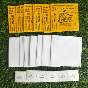 Puede incluir: Un conjunto de tarjetas de felicitaci&oacute;n amarillas de Eid Mubarak con texto &aacute;rabe y un dise&ntilde;o festivo. Las tarjetas est&aacute;n rodeadas de sobres blancos y peque&ntilde;as pegatinas redondas que dicen "Eid Mubarak".