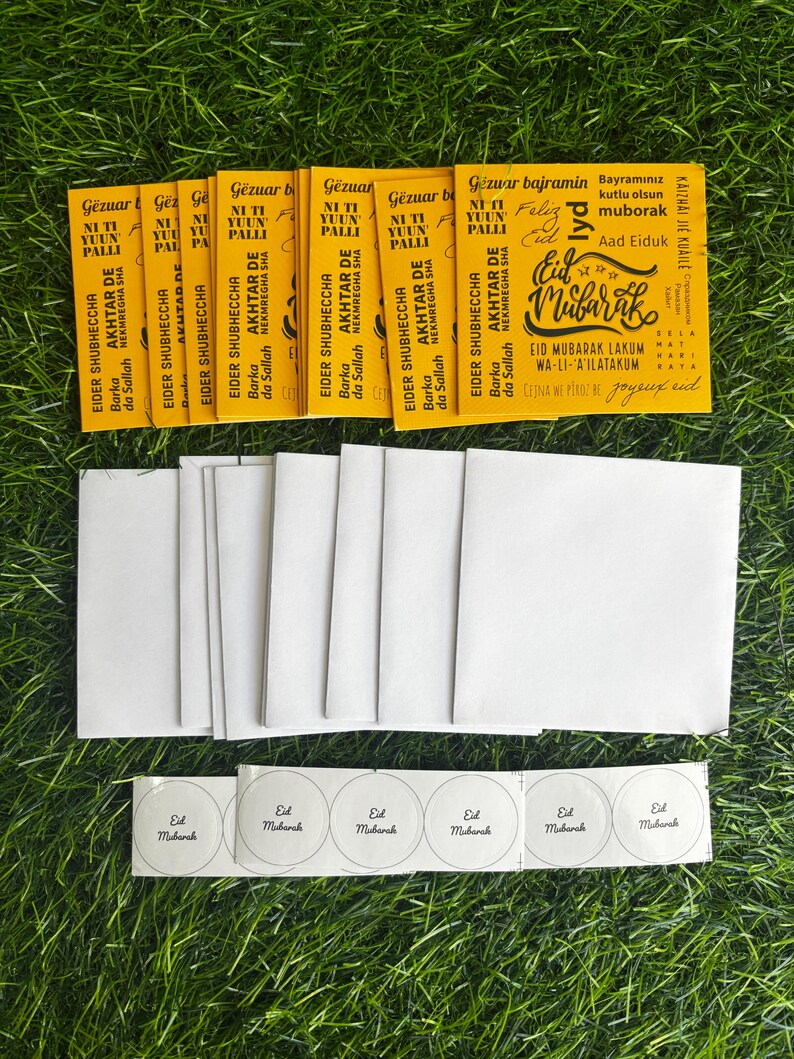Puede incluir: Un conjunto de tarjetas de felicitaci&oacute;n amarillas de Eid Mubarak con texto &aacute;rabe y un dise&ntilde;o festivo. Las tarjetas est&aacute;n rodeadas de sobres blancos y peque&ntilde;as pegatinas redondas que dicen "Eid Mubarak".