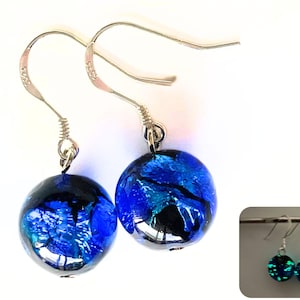 以下が含まれることがあります： 青と黒のガラスビーズが付いたシルバーのドロップイヤリングのペア。ビーズは暗闇で緑色に光ります。