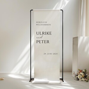Puede incluir: Un cartel de bienvenida blanco con texto negro en un soporte negro. El cartel dice "Herzlich Willkommen Ulrike und Peter 29. Juni 2025".