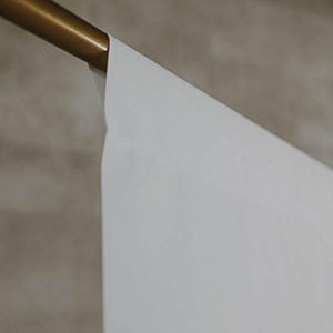 Puede incluir: Un tel&oacute;n de fondo blanco colgado de una varilla de metal dorado. El tel&oacute;n de fondo es liso y sin arrugas.