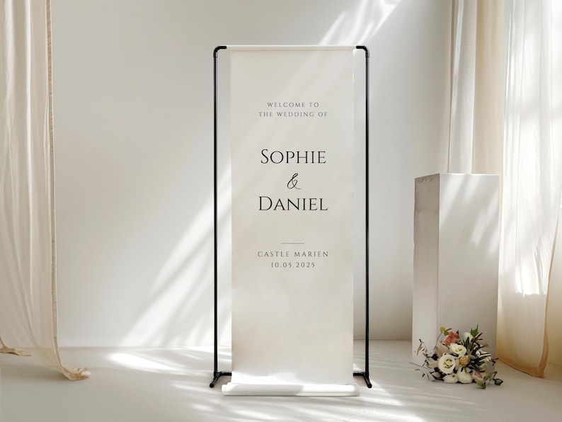 May include: A wedding welcome sign with black frame and a cream-colored banner. The banner reads "Welcome to the wedding of Sophie & Daniel" and includes the date and location.
