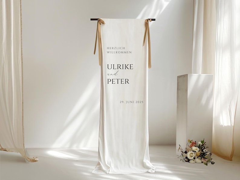 Puede incluir: Tel&oacute;n de fondo de tela blanca con lazos de cinta marr&oacute;n, un letrero que dice "Herzlich Willkommen Ulrike und Peter 29. Juni 2025".