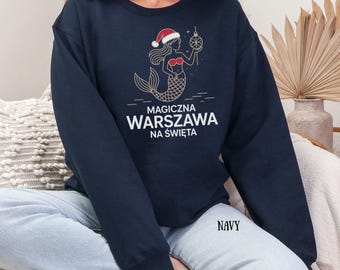 Może przedstawiać: Granatowa bluza z nadrukiem złotej syreny w czapce Świętego Mikołaja, trzymającej bombkę. Tekst "MAGICZNA WARSZAWA NA ŚWIĘTA" jest wydrukowany na biało. Słowo "NAVY" jest wydrukowane w prawym dolnym rogu.
