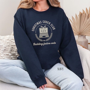 Könnte beinhalten: Marineblaues Sweatshirt mit dem Text "CHRISTMAS CODER CLUB" in einem kreisförmigen Design, mit einer Laptop-Grafik. Der Satz "Building festive code" steht unter der Grafik. Das Wort "NAVY" ist unten aufgedruckt.