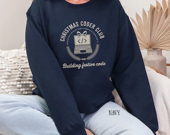 Puede incluir: Sudadera azul marino con el texto "CHRISTMAS CODER CLUB" en un diseño circular, con un gráfico de portátil. La frase "Building festive code" está debajo del gráfico. La palabra "NAVY" está impresa en la parte inferior.