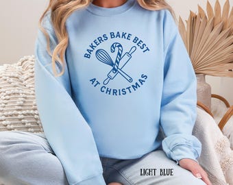 Könnte beinhalten: Hellblaues Sweatshirt mit dem Text "BAKERS BAKE BEST AT CHRISTMAS" in einem kreisförmigen Design. Das Design umfasst einen Schneebesen, eine Teigrolle und eine Zuckerstange. Die Worte "LIGHT BLUE" sind unten aufgedruckt.