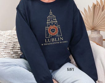 Może przedstawiać: Granatowa bluza z nadrukiem złotego rysunku wieży, wieńca i napisu "LUBLIN". Pod napisem "LUBLIN" znajduje się tekst "W ŚWIĄTECZNYM BLASKU". Słowo "NAVY" jest wydrukowane na dole po prawej stronie.