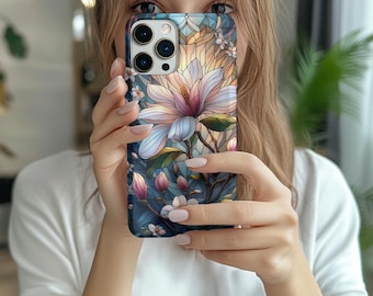 May include: A smartphone case featuring a floral design with a large, light pink and blue magnolia flower. The case has a dark blue background with smaller white flowers and green leaves. The case has a glossy finish.